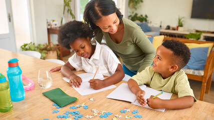 Family Indoors At Home With Mother Helping Children With Homework Sitting At Table