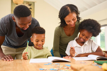 Family Indoors At Home With Parents Helping Children With Homework Sitting At Table