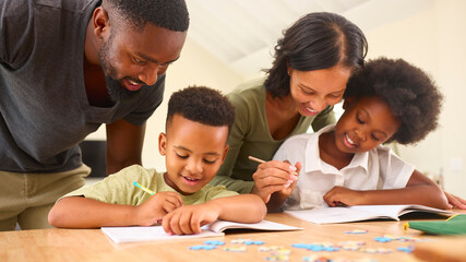 Family Indoors At Home With Parents Helping Children With Homework Sitting At Table