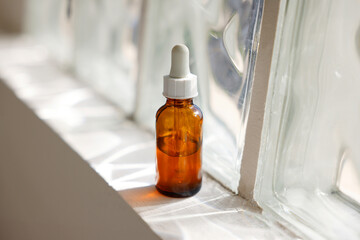 A small brown beauty serum place in the window with sunlight reflection