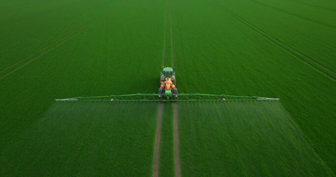 Aerial view of autonomous self-driving tractor with autopilot spraying mineral, nitrogen fertilizer or pesticides on an agricultural field. The agricultural vehicle uses sensors