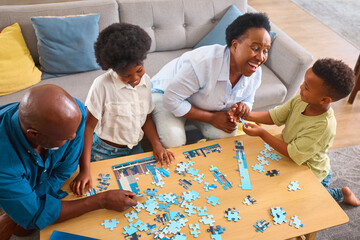 Grandparents With Grandchildren Indoors Sitting Around Table At Home Doing Jigsaw Puzzle Together