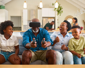 Grandparents With Grandchildren Wearing Virtual Reality Headset Playing Game At Home Together