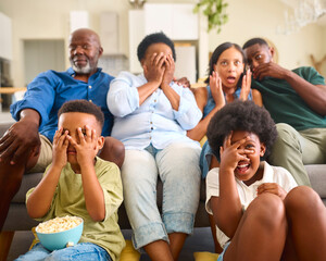 Frightened Multi-Generation Family Sitting On Sofa At Home Watching Horror Movie On TV Together