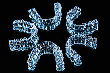 Invisible dental teeth brackets tooth aligners on black background. Plastic braces dentistry retainers to straighten teeth.