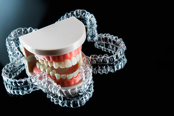 Invisible and removable aligner trays for teeth straightening with artificial jaw lie on a black background