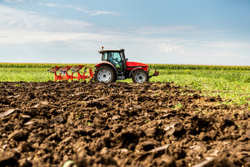 Red tractor plows through fertile soil with a vibrant green landscape in the background