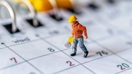 Miniature figure of a construction worker on a calendar, representing project planning or deadlines. - obrazy, fototapety, plakaty