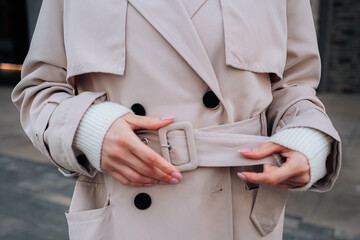 Street style fancy details of a beige women's trench coat with belt. Contemporary urban fashion...