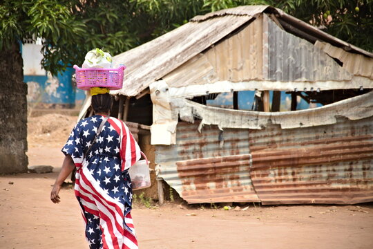 Mujer con vestido llamativo de bandera americana portando barreño en la cabeza en un pueblo africano