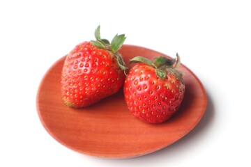 Fresh strawberries in a wooden bowl on a white background.
