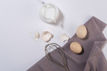 Minimals cooking style with a dark gray towel decorated on white background next to some eggs, a cup of milk and a whisk to mix egg. Cooking layout for bakery or restaurant advertising