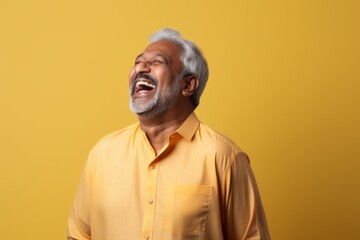 Obraz premium Portrait of a joyful indian man in his 60s sporting a long-sleeved thermal undershirt on pastel yellow background