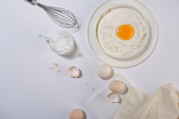 Flat lay composition with various ingredients for baking or cooking on minimals white background with eggs, flour and milk. Copy space for adding text or elements of designing