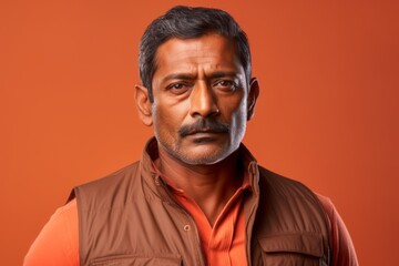 Portrait of a tender indian man in his 40s dressed in a thermal insulation vest while standing against pastel orange background