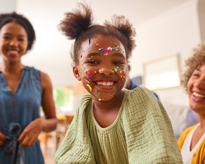 Granddaughter With Face Decorated With Party Glitter With Grandmother With Mother At Home Together