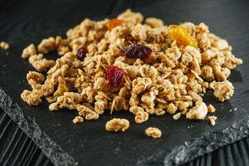 tasty crunchy granola with dried fruits on a black wooden rustic background