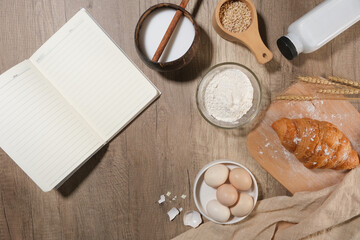 A blank notebook opened beside ingredients for baking cake or pastry flat lay on wooden kitchen counter top. Space for designing, top view