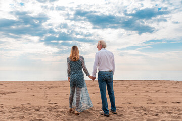 Mature couple holding hands on beach at sunset - 787068542