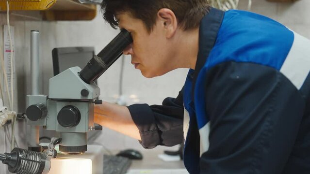 Scientist in uniform using a microscope in a lab for research and analysis. Chemist assistant worker in chemical laboratory testing hypothesis. Scientific optical equipment 