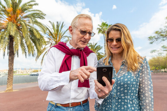 Happy senior couple portrait at seaside in Barcelona using mobile phone