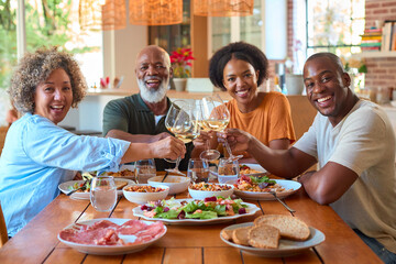 Portrait Of Senior Parents Around Table Eating Meal With Wine At Home With Adult Son And Daughter