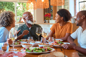 Senior Parents Around Table Eating Meal With Wine At Home With Adult Son And Daughter
