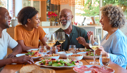 Senior Parents Around Table Eating Meal With Wine At Home With Adult Son And Daughter