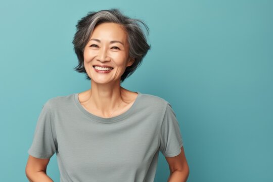 Portrait of a satisfied asian woman in her 60s dressed in a casual t-shirt while standing against soft blue background