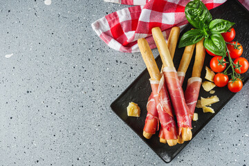 crispy grissini with prosciutto on a light stone background