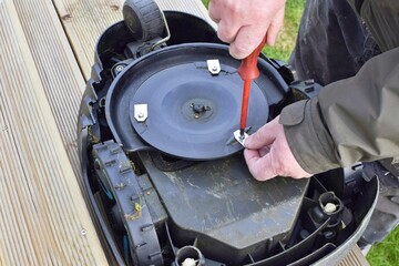 Man swaps blades for robotic lawn mower