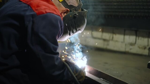 A skilled welder fuses metal with a welding torch with sparks in an industrial setting. Factory worker from metallurgy production plant.