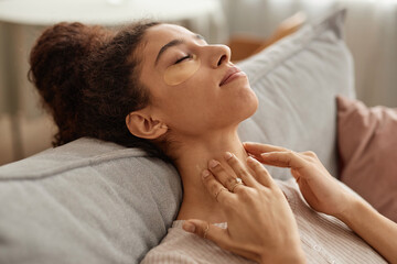 Side view portrait of blissful young woman enjoying self care day at home and doing face and neck massage copy space