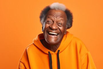 Portrait of a grinning afro-american man in his 80s wearing a thermal fleece pullover in front of soft orange background