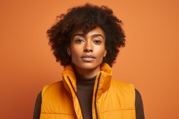 Obraz na płótnie Canvas Portrait of a glad afro-american woman in her 20s dressed in a water-resistant gilet isolated on soft orange background