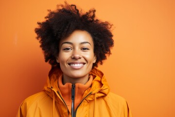Obraz na płótnie Canvas Portrait of a glad afro-american woman in her 20s dressed in a water-resistant gilet in front of soft orange background