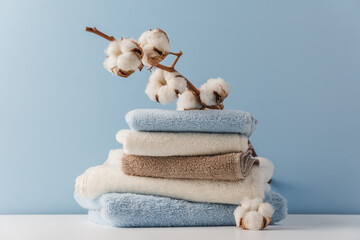Stack of delicate colored cotton towels with cotton buds on blue background