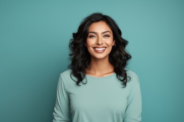 Fototapeta premium Portrait of a satisfied indian woman in her 30s sporting a long-sleeved thermal undershirt on soft teal background