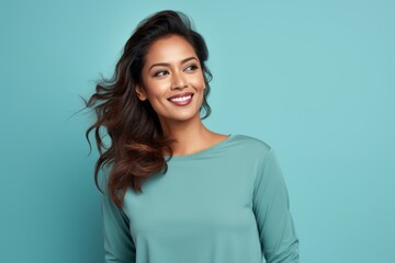 Portrait of a satisfied indian woman in her 30s sporting a long-sleeved thermal undershirt while standing against soft teal background