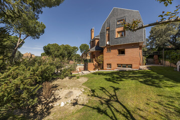 Fototapeta premium Estate with a chalet with a characteristic black slate roof, a large garden with grass, hedges and abundant trees