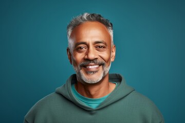 Portrait of a merry indian man in his 50s dressed in a comfy fleece pullover while standing against soft teal background