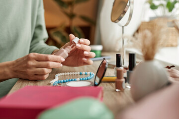 Close up of female hands holding nude nail polish bottle while doing manicure at home copy space