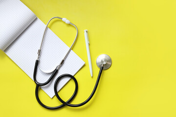 Stethoscope, notepad and pen on a yellow background, top view. Cardiology and healthcare concept. Auscultation device. Medical care concept. Medical instrument. Auscultation apparatus