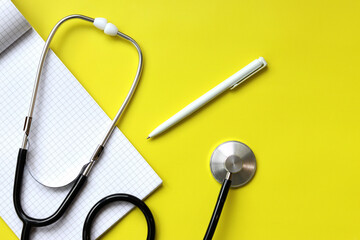 Stethoscope, notepad and pen on a yellow background, top view. Cardiology and healthcare concept....
