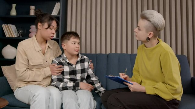 Worried affectionate African American mother and adorable school age black son with adolescent problems counselling with attentive lovely psychologist, to improve social skills indoors.