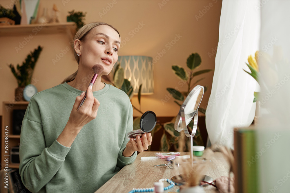 Wall mural portrait of elegant young woman doing make up looking in mirror by window copy space