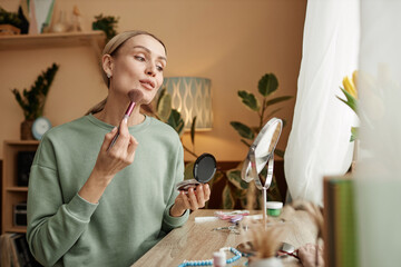 Portrait of elegant young woman doing make up looking in mirror by window copy space - 787087175