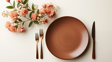 Table setting with thick brown ceramic plate, cutlery and flowers on white background