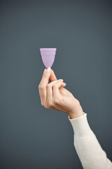 Vertical shot of female hand holding pink silicone menstrual cup on blue background copy space - 787099747