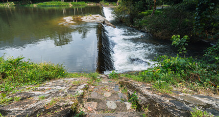 Small dam with water flowing rapids. Seen as lines and patterns with foam. The natural river abundant and surrounded by forest.